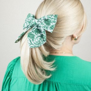 Frau mit blondem Pferdeschwanz und grün-weiß gemusterter Haarschleife